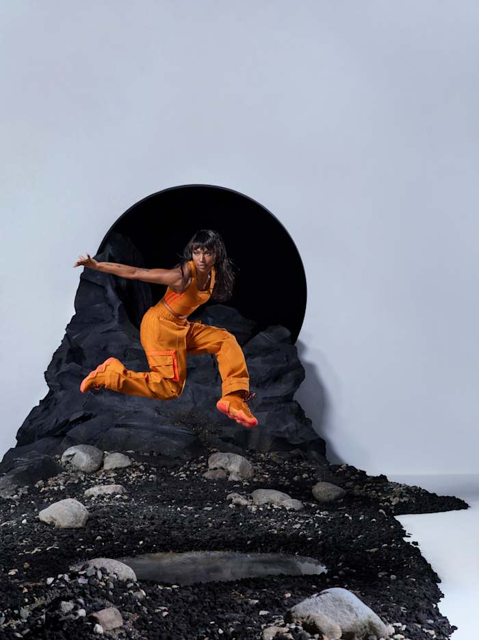 Woman wearing orange adidas clothing jumping in photo shoot.